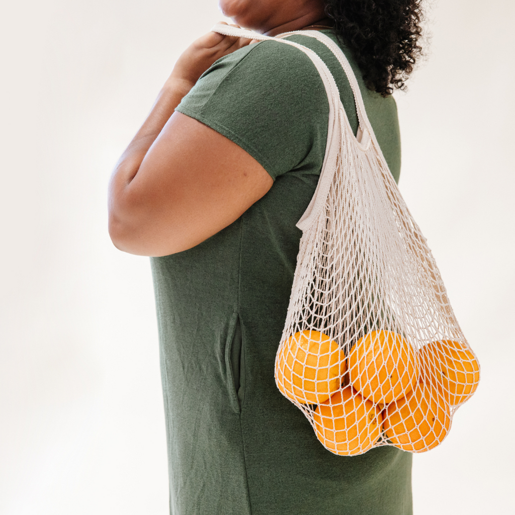 person wearing green top carries string bag filled with oranges